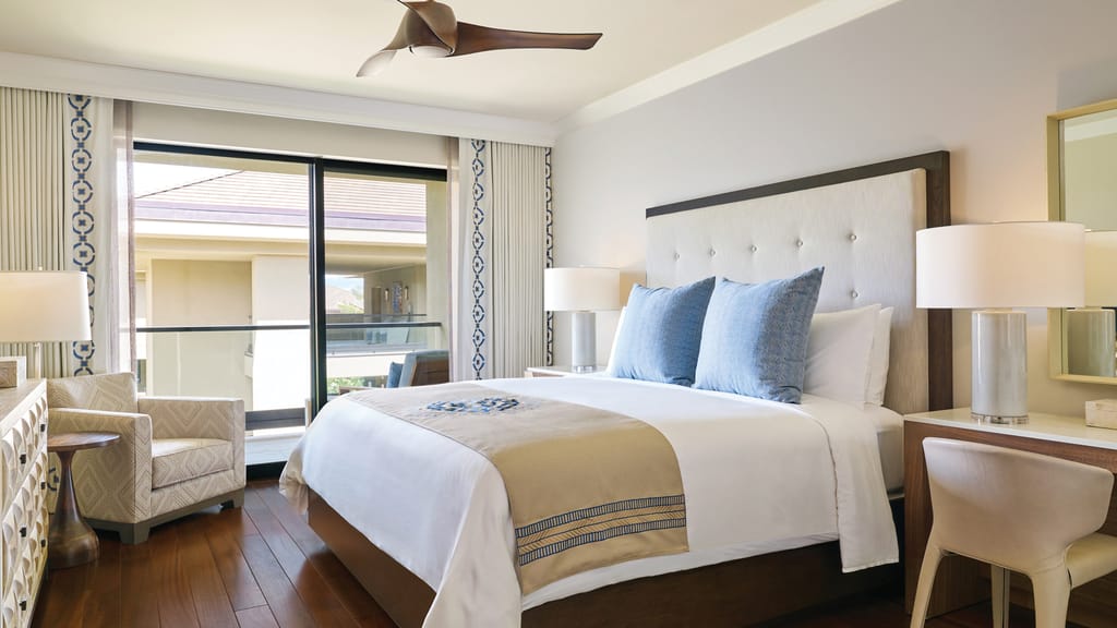 A wide view of a hotel room with a bed, desk, chair, and lamp.