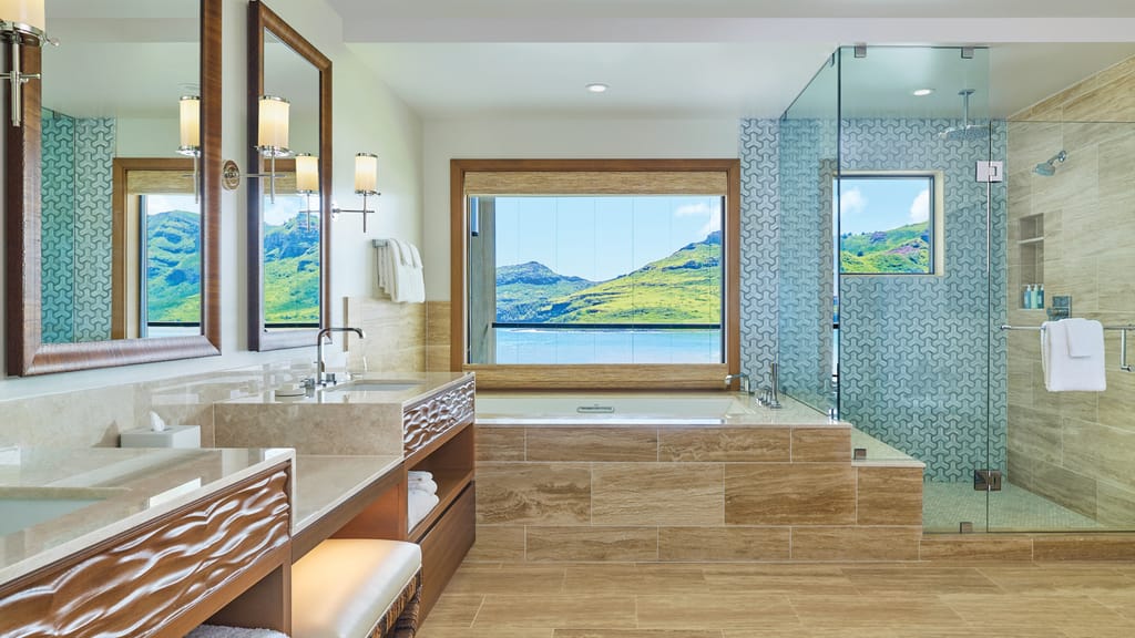 A modern bathroom with a bathtub, shower, double sink, and a large window with a scenic view.