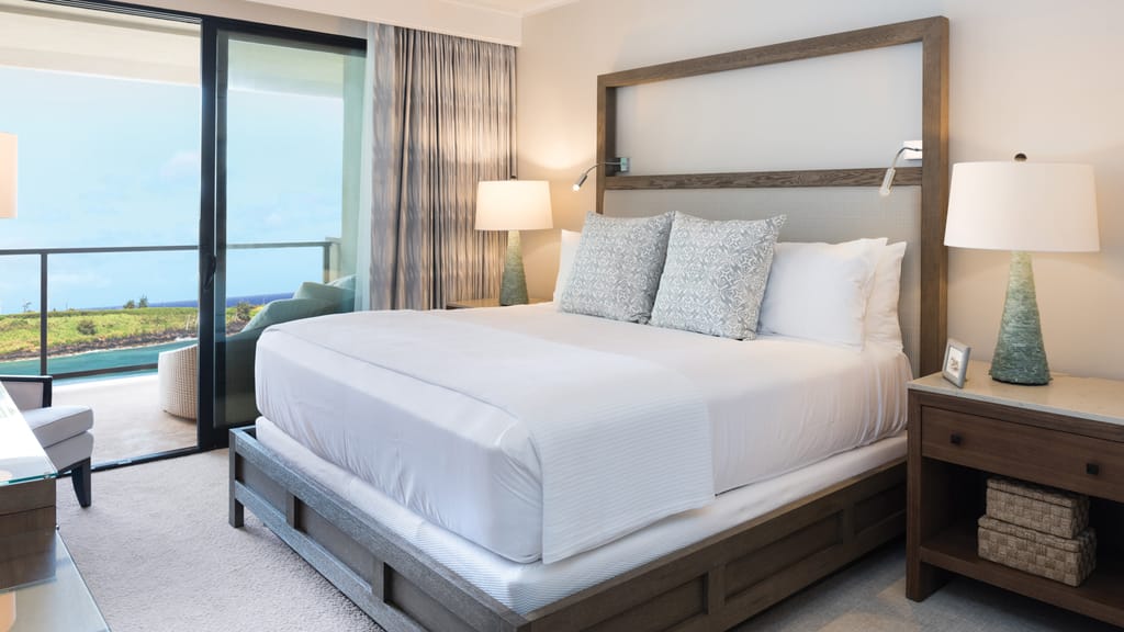 A hotel room with a large bed, nightstand, and balcony with a view.