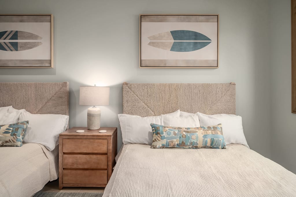 A hotel room with two twin beds, a wooden nightstand, and surfboard artwork on the wall.
