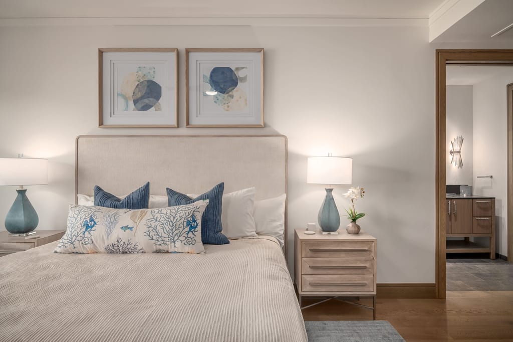 A neatly made bed with blue and white pillows and a framed artwork above it.