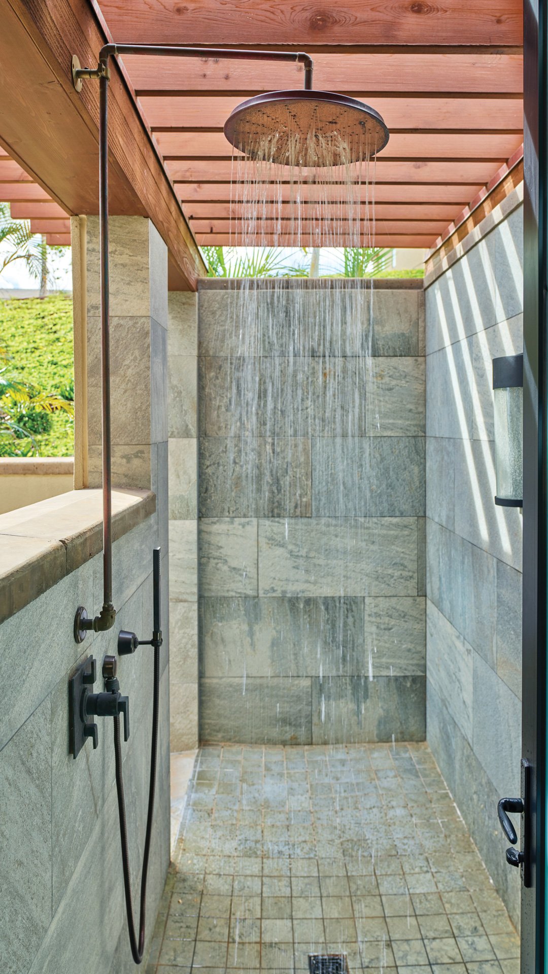 An outdoor shower with a rain showerhead and stone walls