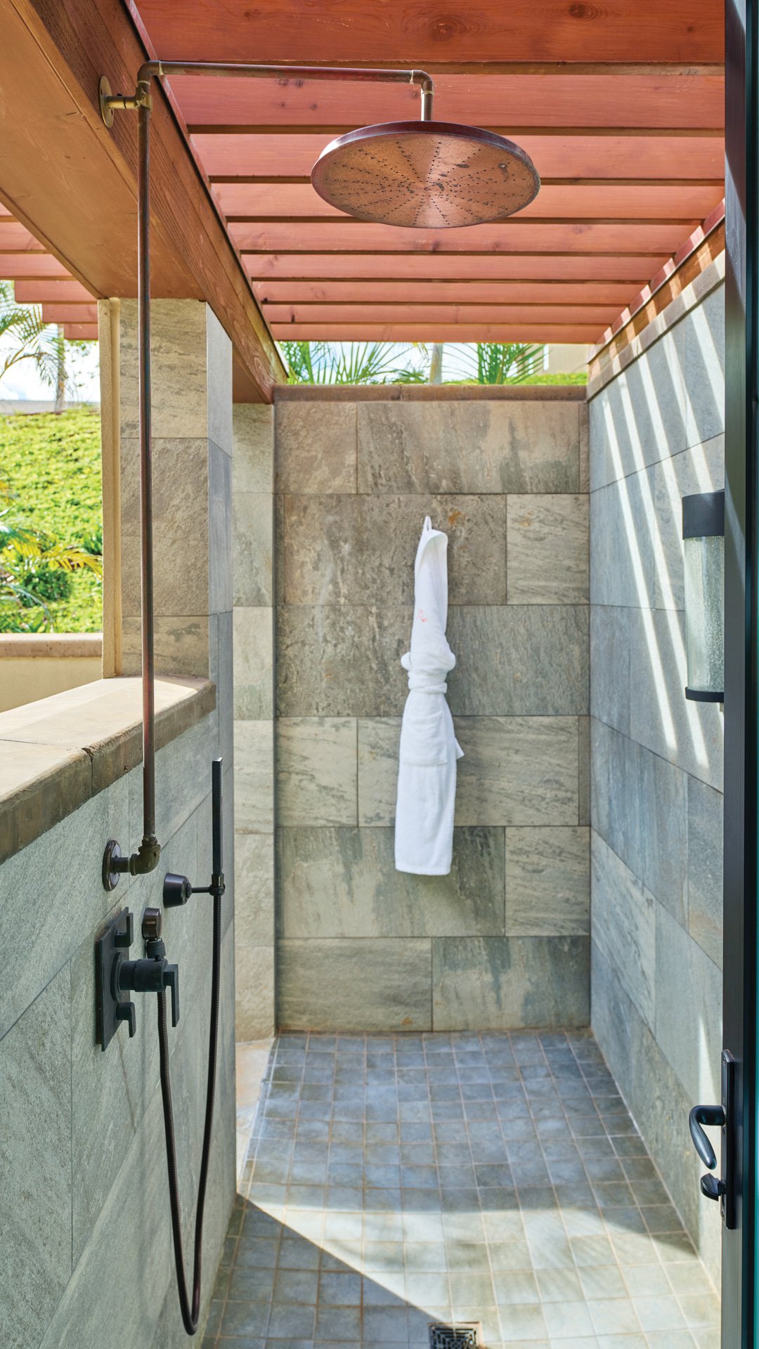 An outdoor shower with a rain showerhead and stone tile walls under a wooden ceiling