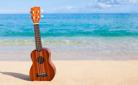 Ukulele on beach in front of blue sea.