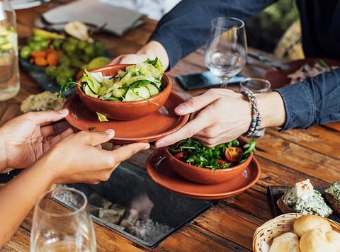 two people hold a shared dish of fresh cut vegetables in a salad bowl