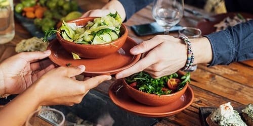 two people hold a shared dish of fresh cut vegetables in a salad bowl